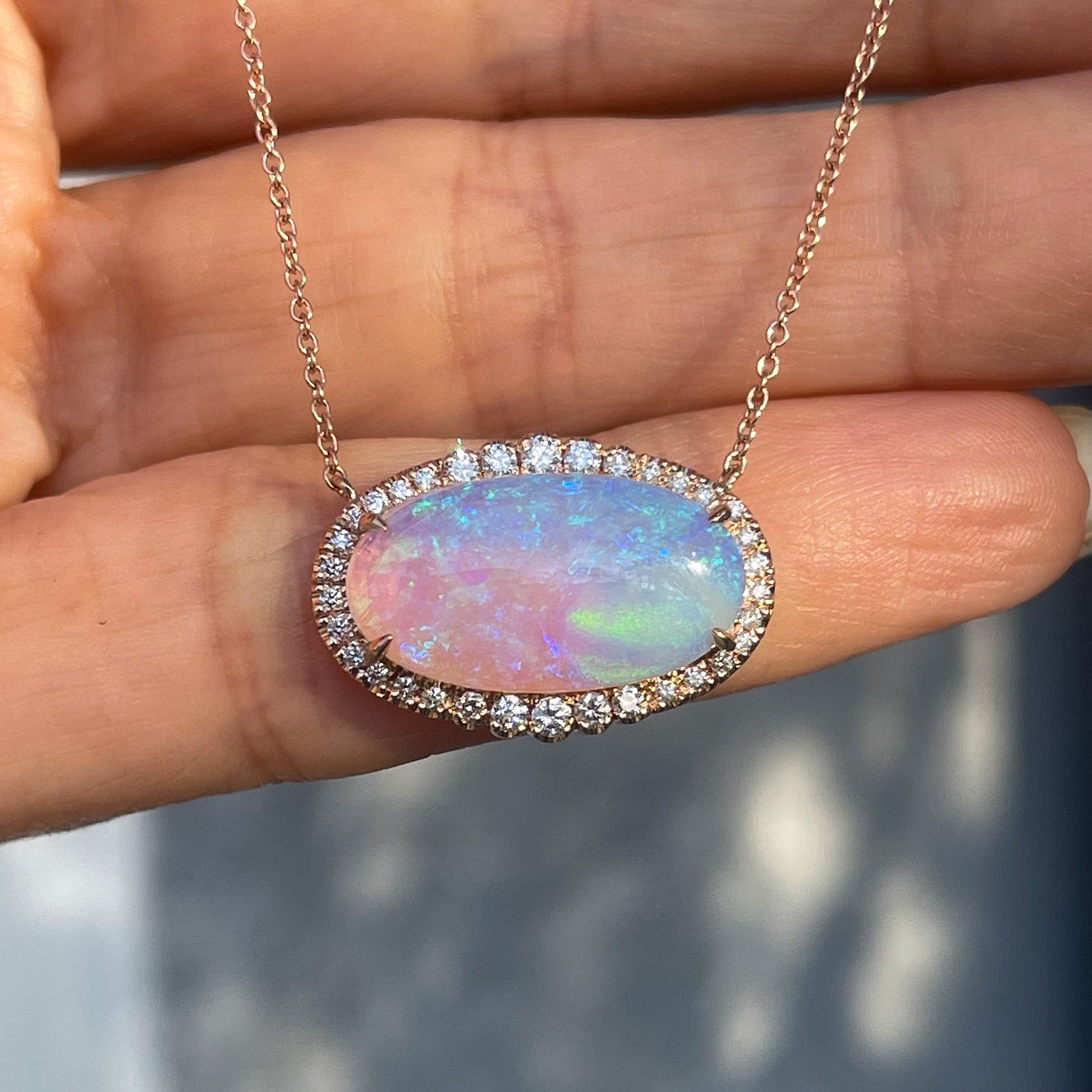 An Australian Opal Necklace by NIXIN Jewelry resting on a hand. The purple and blue opal necklace is set in 14k rose gold.