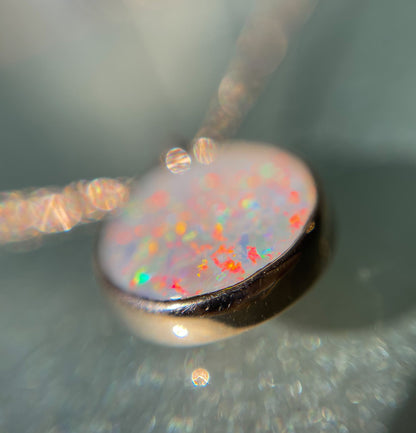 A magnified image of an Australian Opal Necklace by NIXIN Jewelry shot from the base of the bezel setting. The rose gold opal necklace is resting on a table.