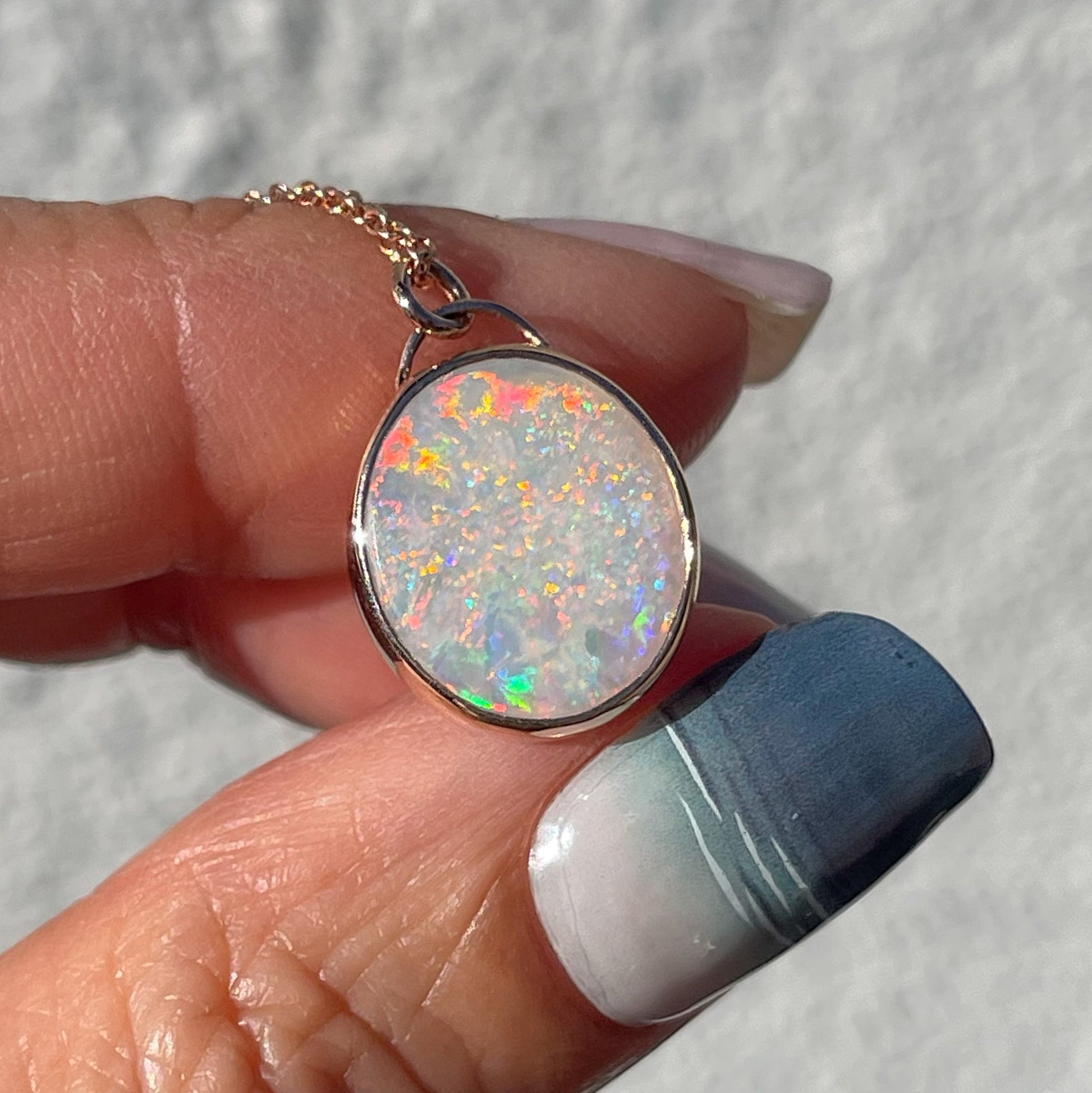 An Australian Opal Necklace by NIXIN Jewelry with a Coober Pedy Opal set in a rose gold. The Australian Opal Pendant is held up in the sunlight.