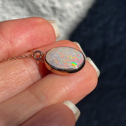 An Australian Opal Necklace by NIXIN Jewelry sitting flat on its back, atop a model's hand, displaying its bezel setting and bail.