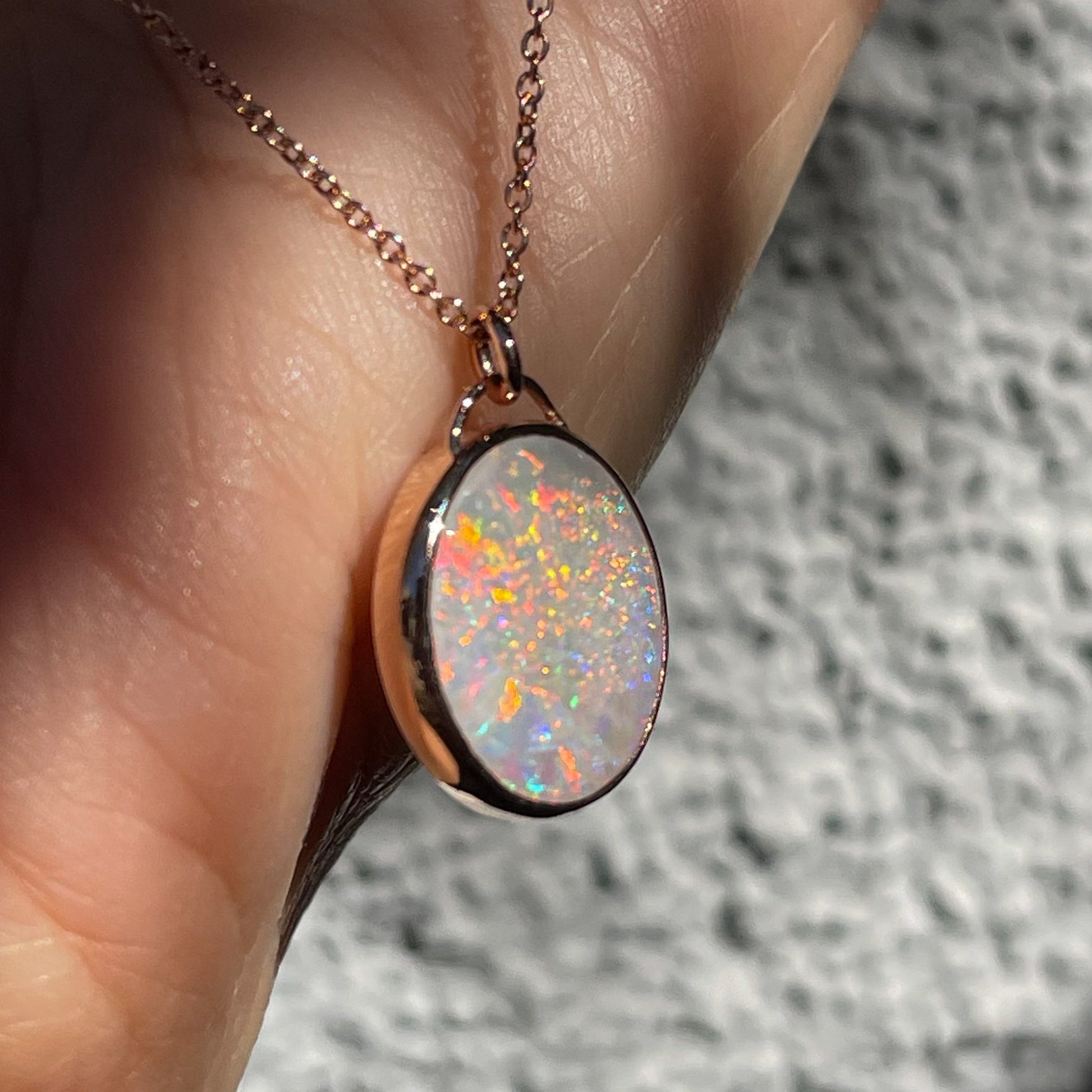 Angled shot of an Australian Opal Necklace by NIXIN Jewelry showing the side of the rose gold bezel setting. The opal pendant is resting against a hand.