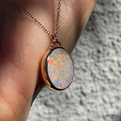 Angled shot of an Australian Opal Necklace by NIXIN Jewelry showing the side of the rose gold bezel setting. The opal pendant is resting against a hand.
