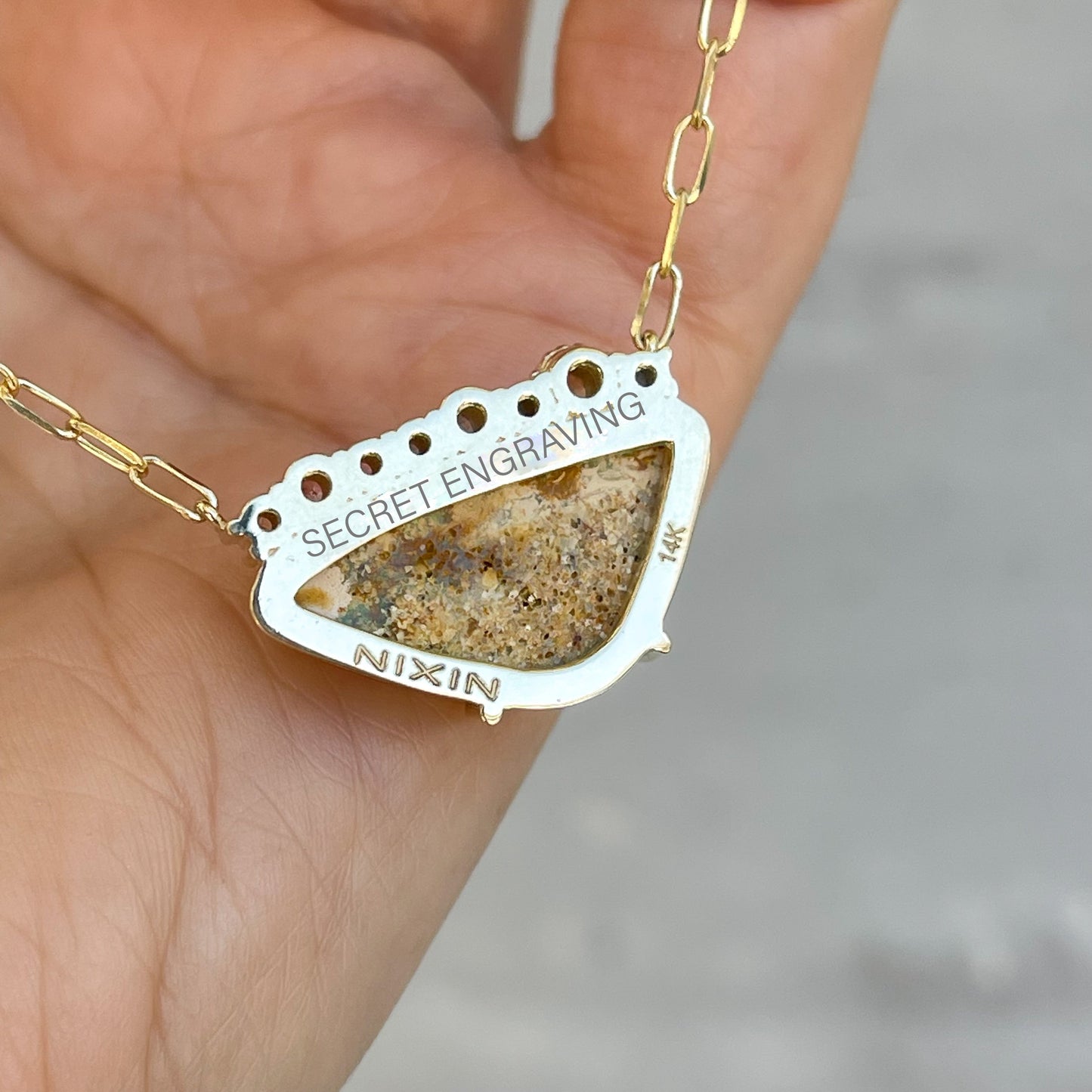 An Australian Opal Necklace by NIXIN Jewelry with a secret engraving on the back. This photo of the opal pendant resting on the hand shows where the secret inscription is.