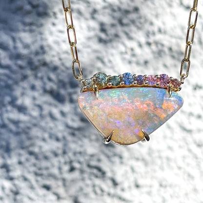 An Australian Opal Necklace by NIXIN Jewelry set in 14k yellow gold hangs in front of a grey wall.