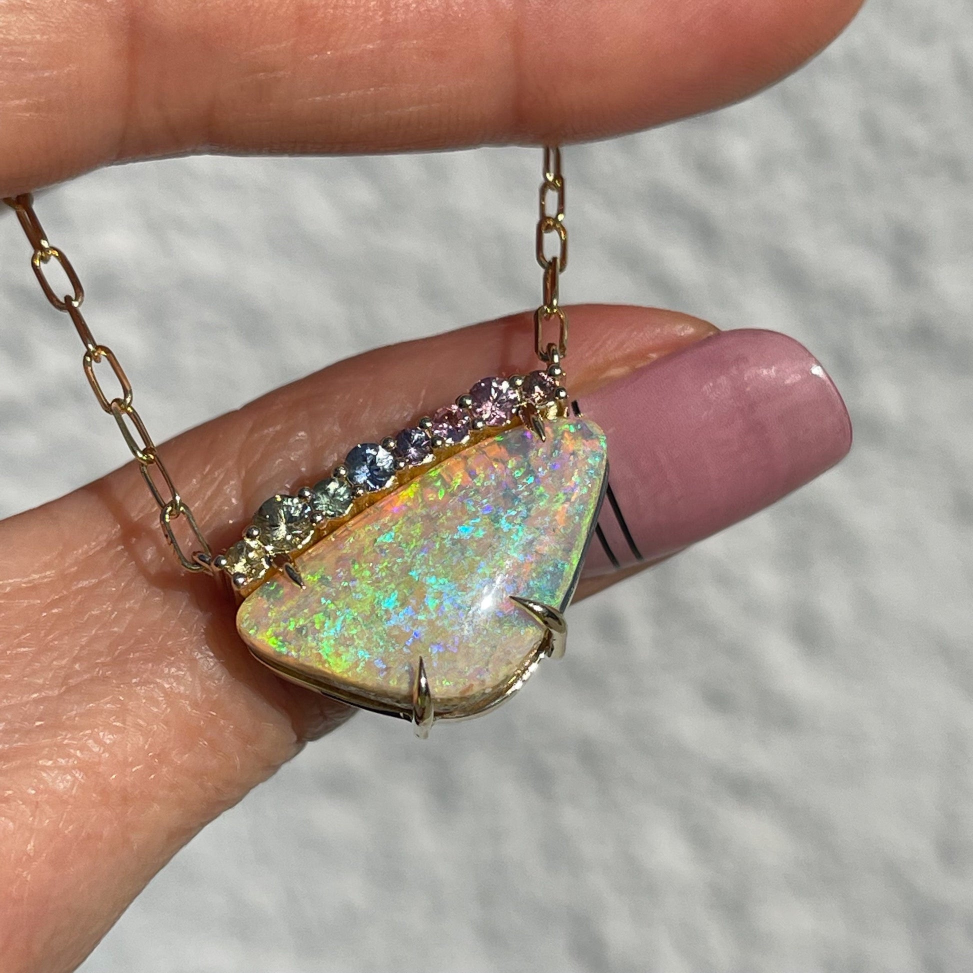 An Australian Opal Necklace by NIXIN Jewelry. The opal sapphire necklace is resting on a hand in the sunlight.