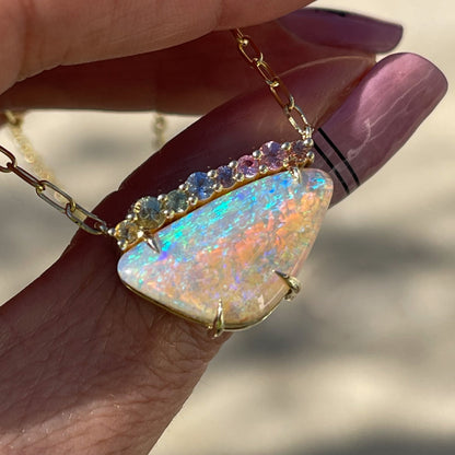 An Australian Opal Necklace by NIXIN Jewelry rests atop a finger. A Crystal Opal necklace with sapphires set in 14k gold.