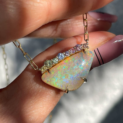 An Australian Opal Necklace by NIXIN Jewelry is shown resting on the hand and spotlit in sunlight. The opal necklace hangs from a gold paperclip chain.