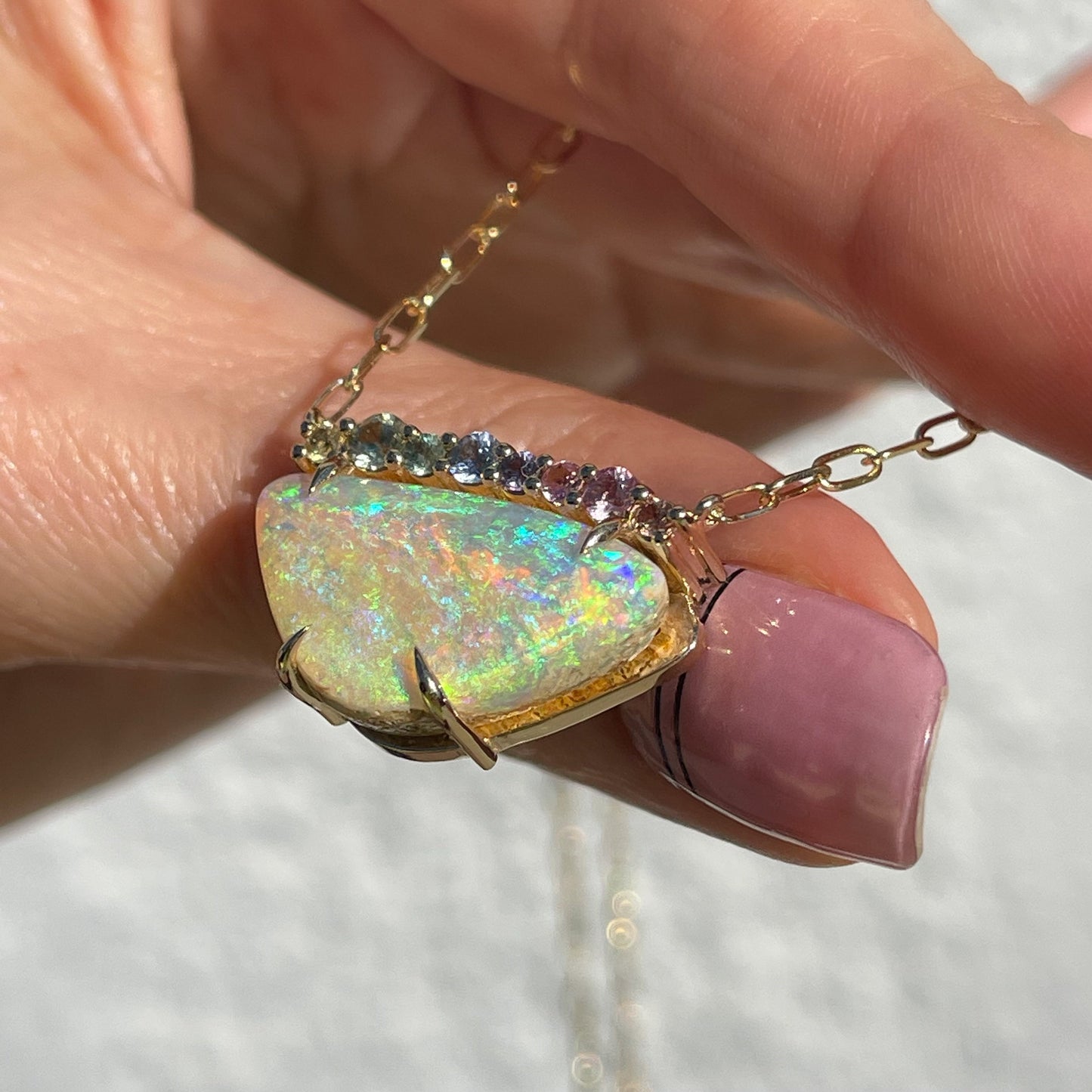 An Australian Opal Necklace by NIXIN Jewelry. The Crystal Opal necklace is set in gold and shot at an angle to show the side of the necklace as it rests on a finger.