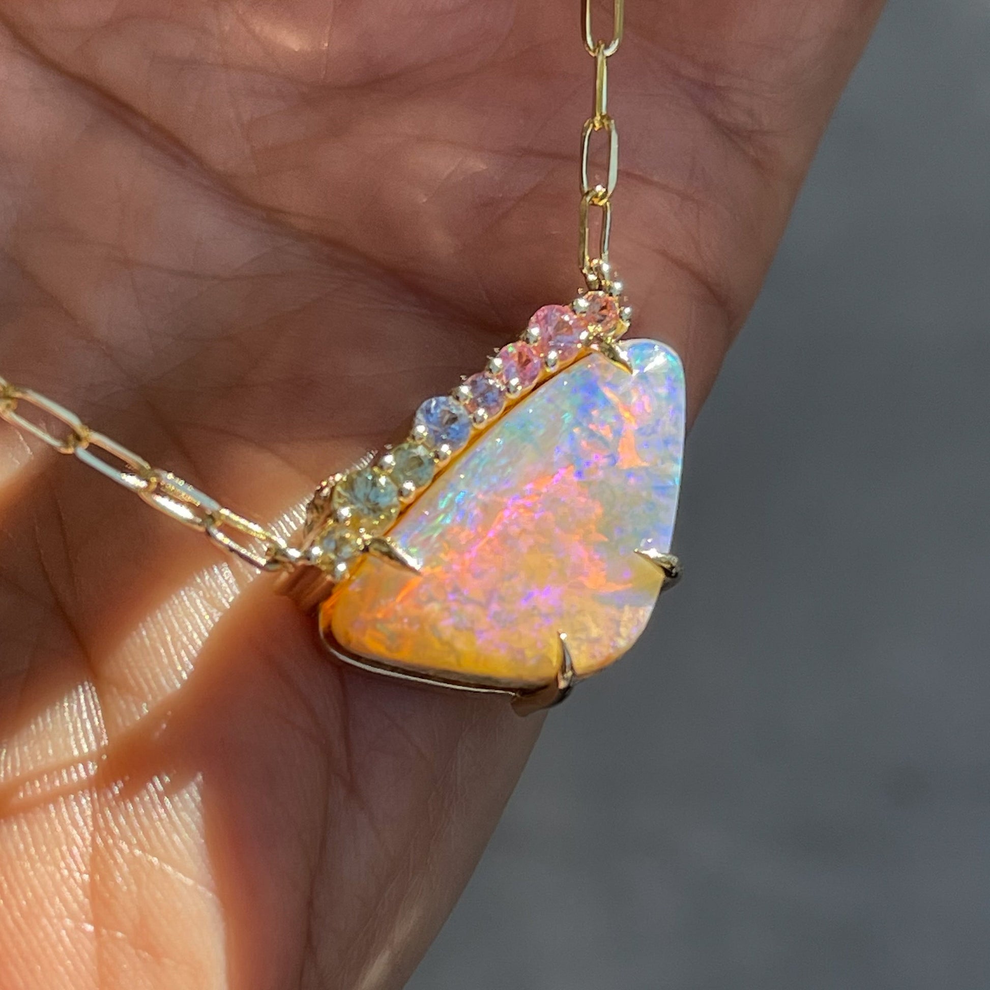 An Australian Opal Necklace by NIXIN Jewelry is shown resting on a hand, as the opal and sapphires sparkle in the sun.