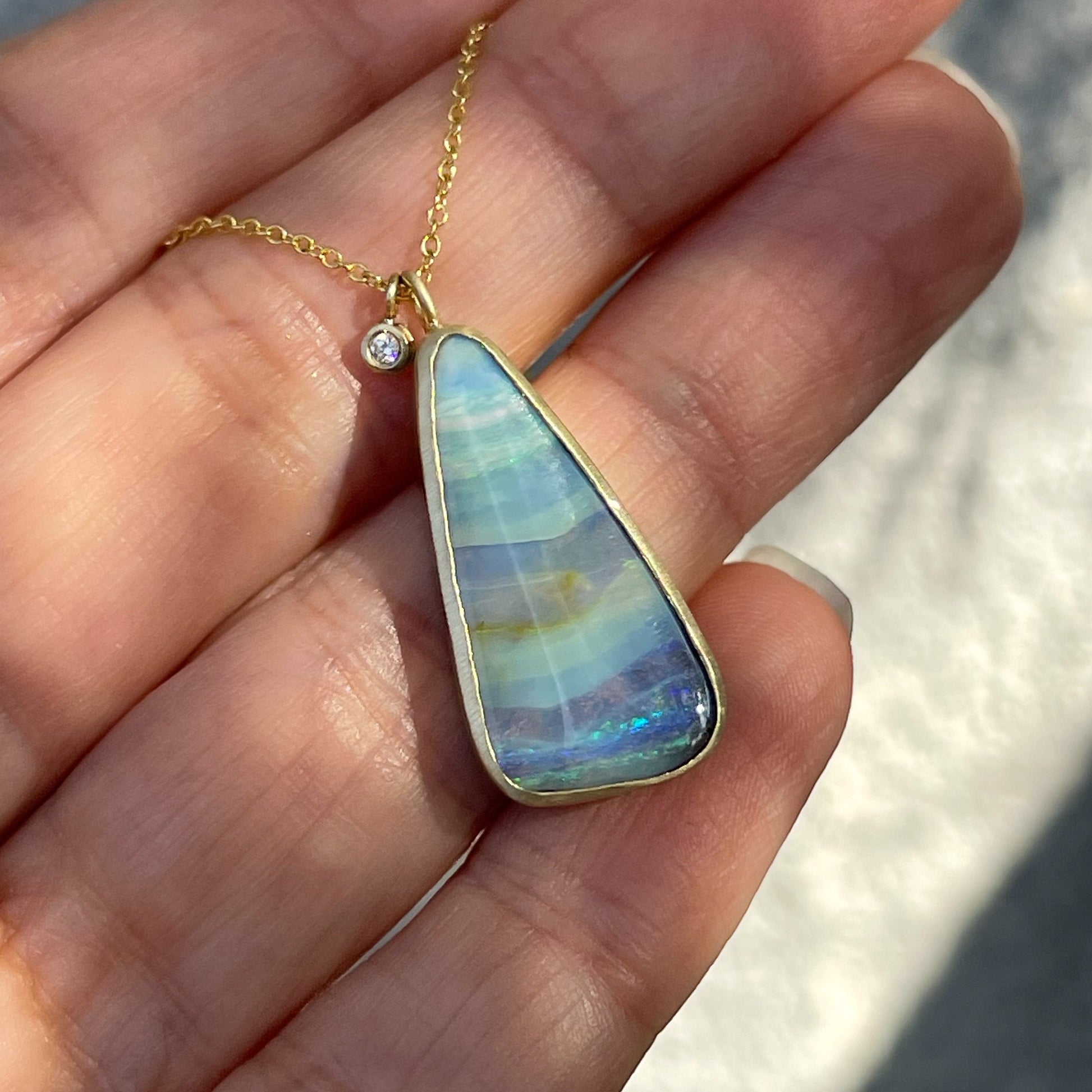 Opal and diamond necklace by NIXIN Jewelry shown against hand