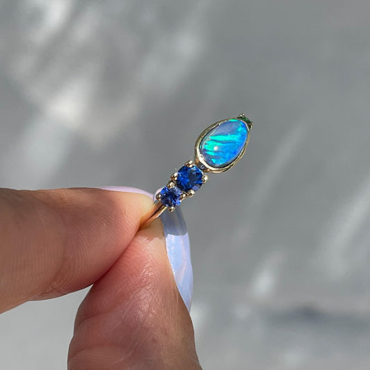 Black Opal Ring by NIXIN Jewelry held showing side. Gold opal ring with sapphires.
