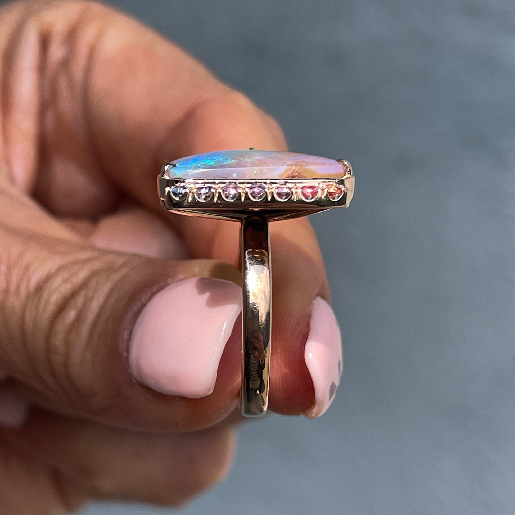 A profile shot of an Australian Opal Ring by NIXIN Jewelry. The opal and sapphire ring has a pink and blue opal next to pink to blue ombré sapphires. 