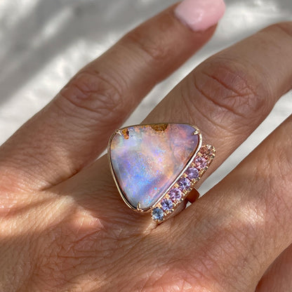 An Australian Opal Ring by NIXIN Jewelry modeled on a hand. The rose gold opal ring is prong set with sapphires down the side.