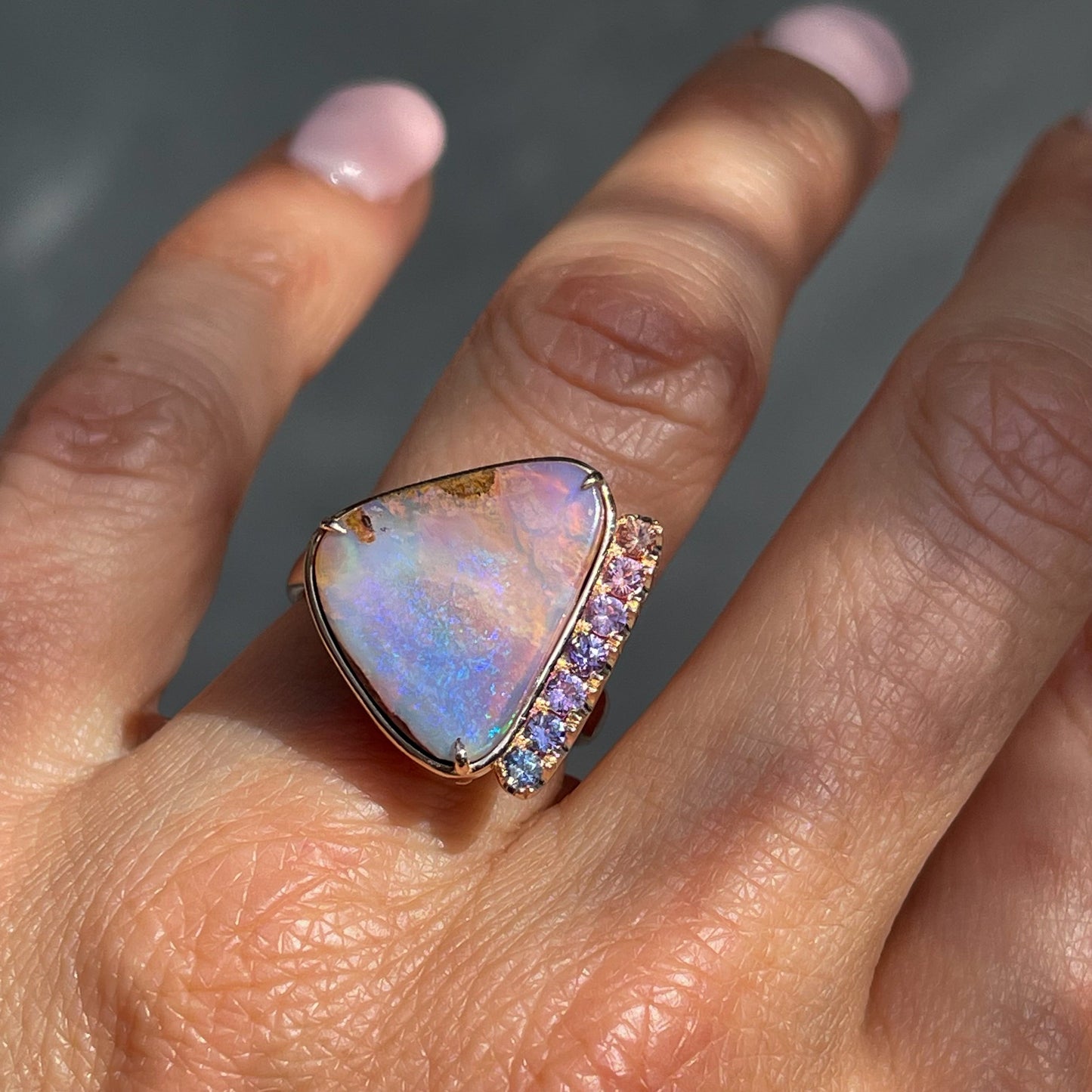 An Australian Opal Ring by NIXIN Jewelry modeled on a hand. The rose gold opal ring is a one of a kind piece of jewelry — a form of opal art.