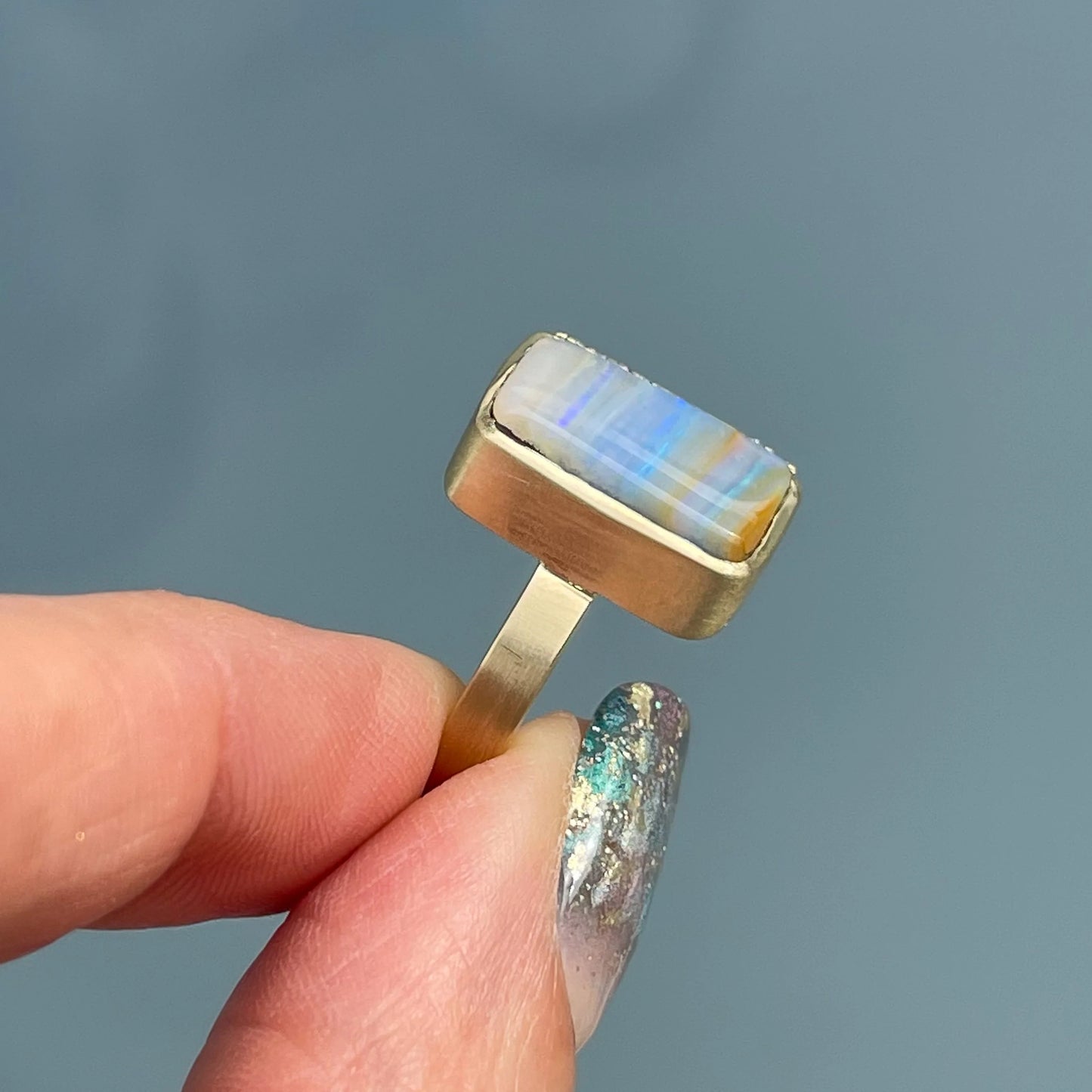 An Australian Opal Ring by NIXIN Jewelry with a Boulder Opal set in yellow gold is held to show the side of its bezel setting.