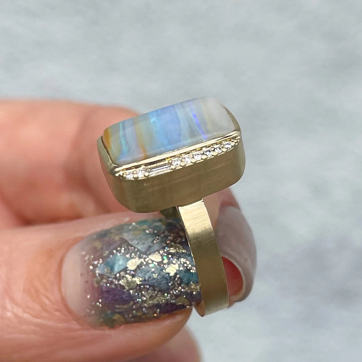 An Australian Opal Ring by NIXIN Jewelry with a striped opal is held to show its diamond border.