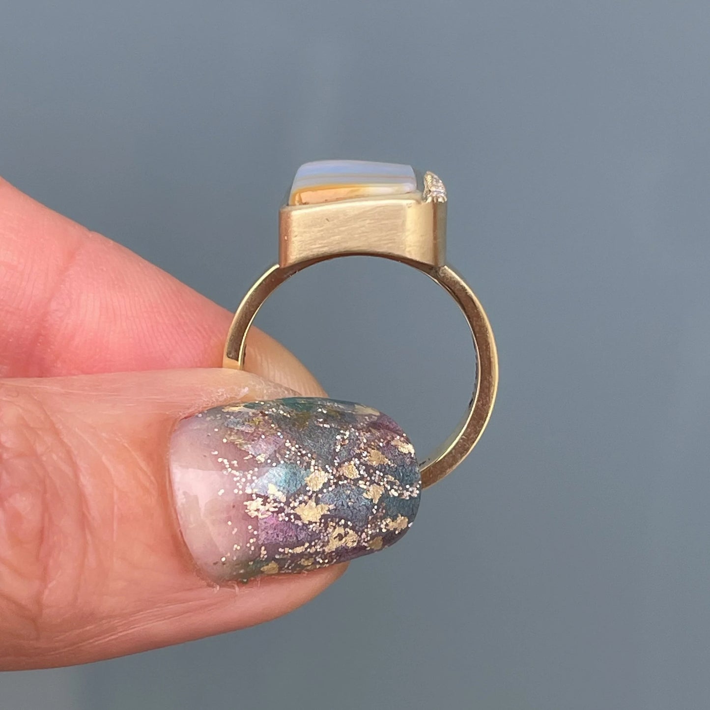 An Australian Opal Ring by NIXIN set in 14k yellow gold held to show side view.