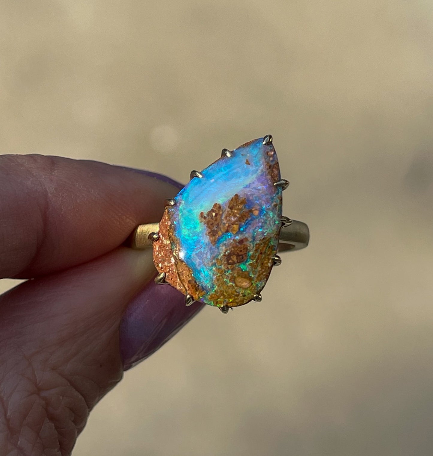 A NIXIN Jewelry Australian Opal Ring is held up in late afternoon sunlight displaying its bold purple and blue hues. 