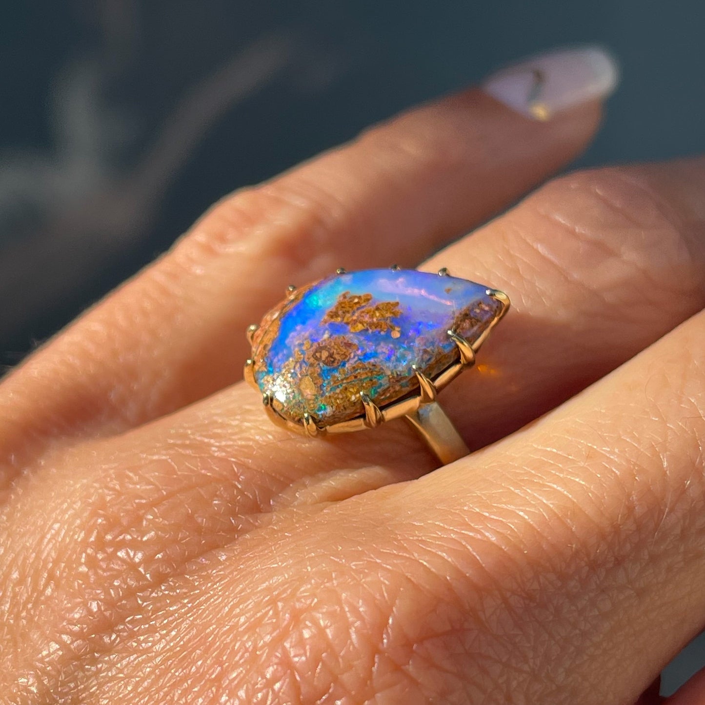 A NIXIN Jewelry Australian Opal Ring modeled on a hand and shot at a slight angle displaying the band and claw prong setting.
