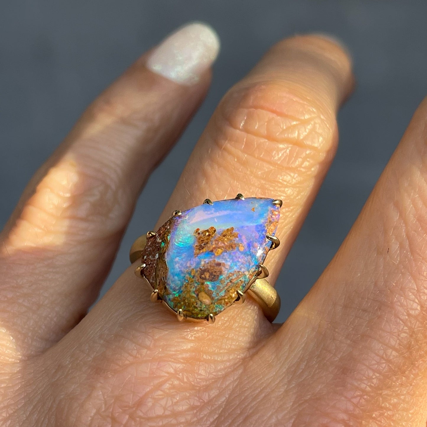 A NIXIN Jewelry Australian Opal Ring mounted in a 14k yellow gold prong setting. The natural opal ring is modeled on a hand.