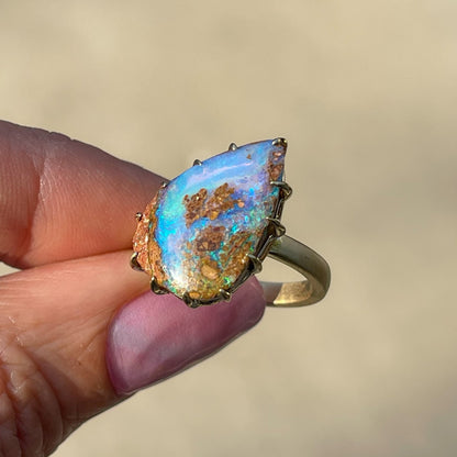 A NIXIN Jewelry Australian Opal Ring held at an angle to show the side of the prong setting and band. Made with an Australian Boulder Opal.