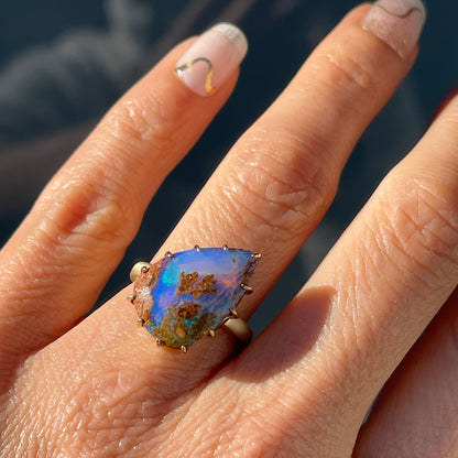 A NIXIN Jewelry Australian Opal Ring modeled on a hand. The lighting reveals the depth of the Australian Boulder Opal.