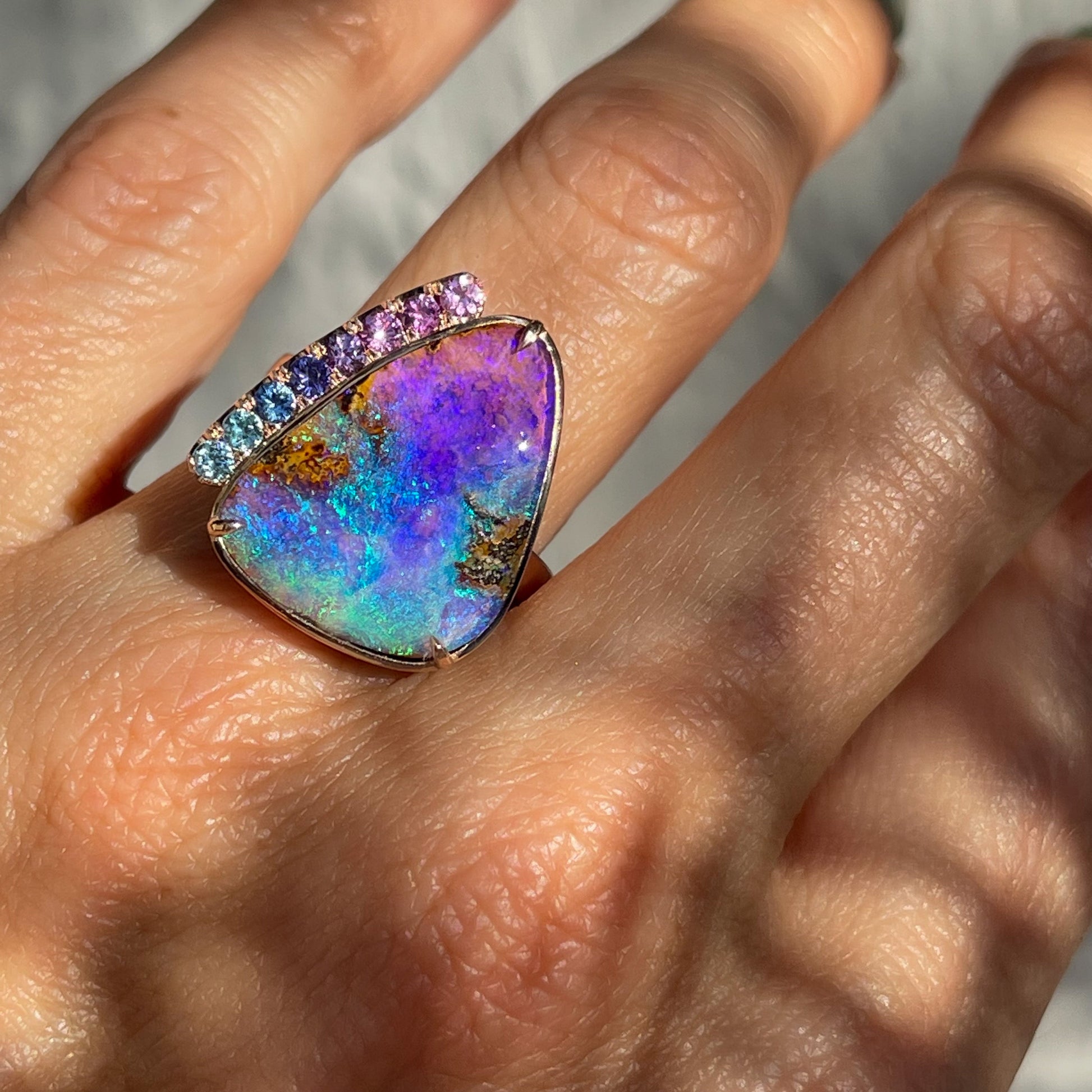 An Australian Opal Ring by NIXIN Jewelry featuring a purple and green opal is modeled on the hand.