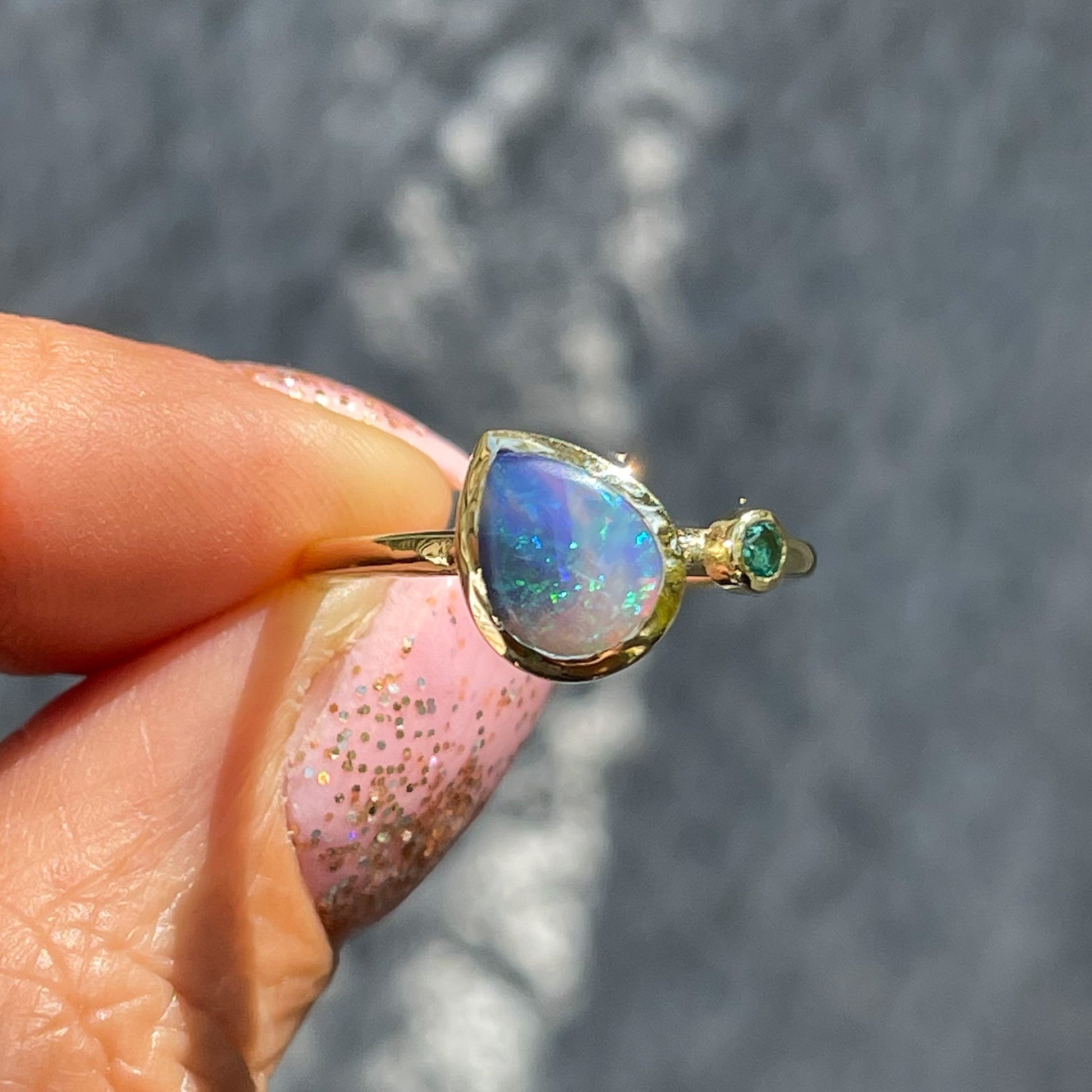 An Australian Opal Ring by NIXIN Jewelry held in sunlight. A natural opal ring made with a Black Opal.