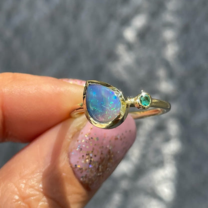 An Australian Opal Ring by NIXIN Jewelry held in sunlight. Made in yellow gold with a Lightning Ridge Opal and emerald.