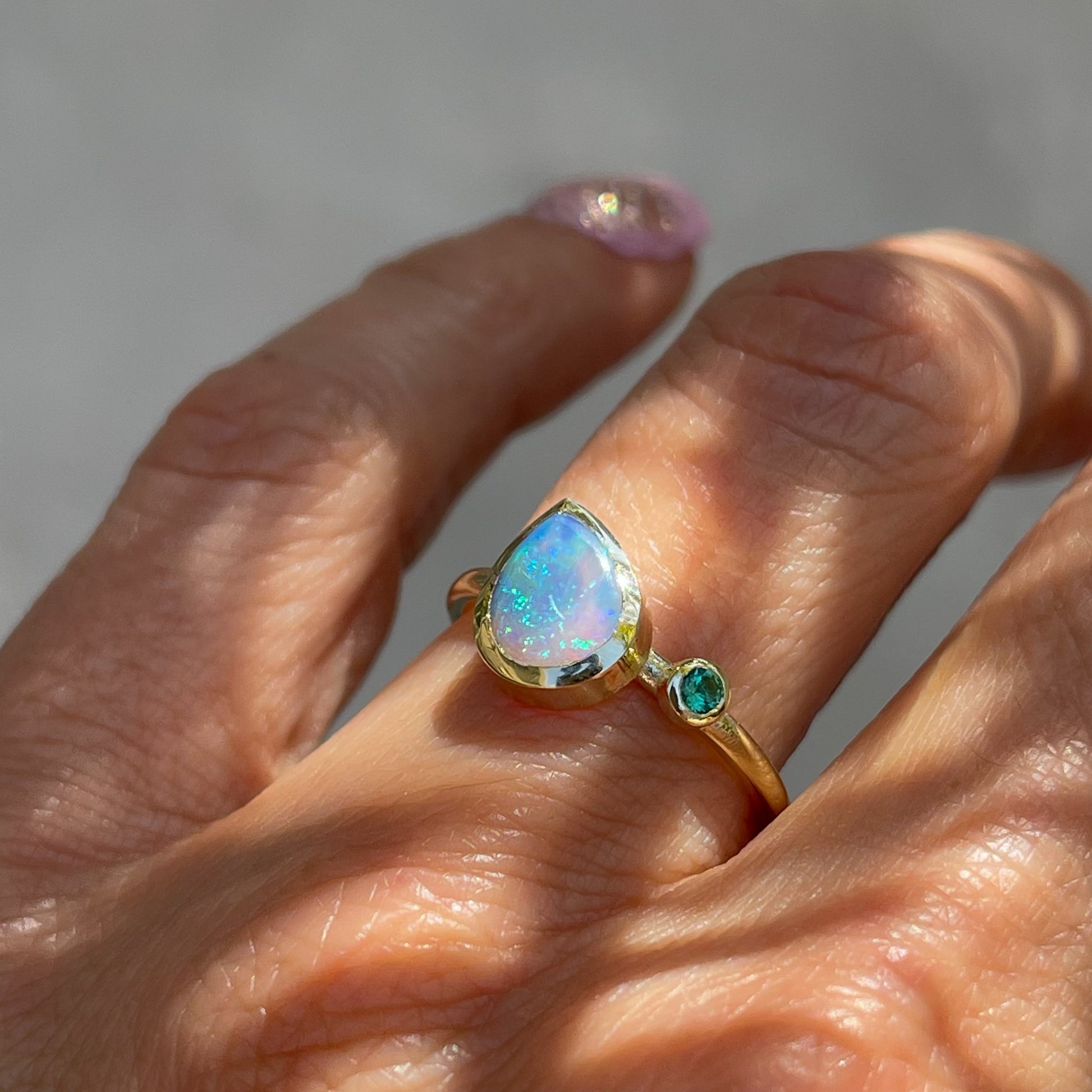 An emerald and Australian Opal Ring by NIXIN Jewelry modeled on the hand. Made with a Black Crystal Opal in 14k gold.
