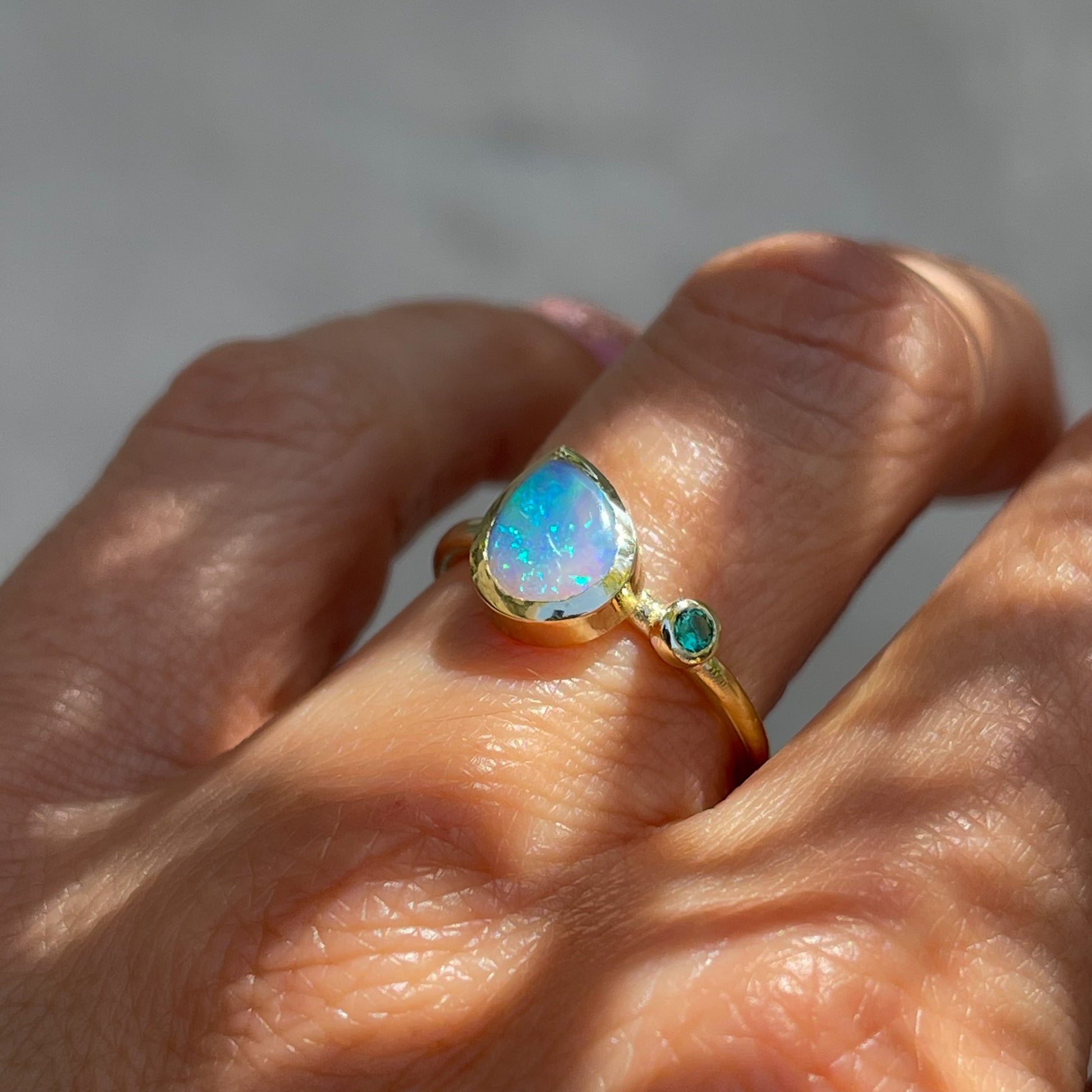 An Australian Opal Ring by NIXIN Jewelry modeled on a hand. Made with a Black Crystal Opal and an emerald in 14k yellow gold.