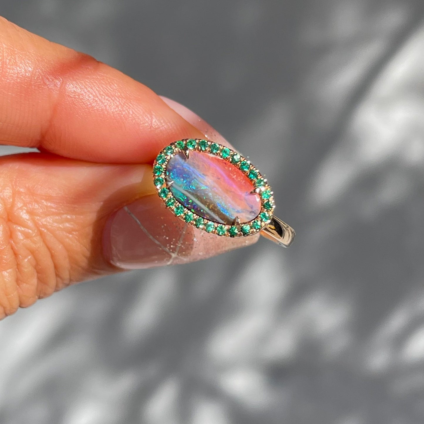 Australian Opal and Emerald Ring by NIXIN Jewelry held in sunlight. Australian boulder opal ring with emeralds.