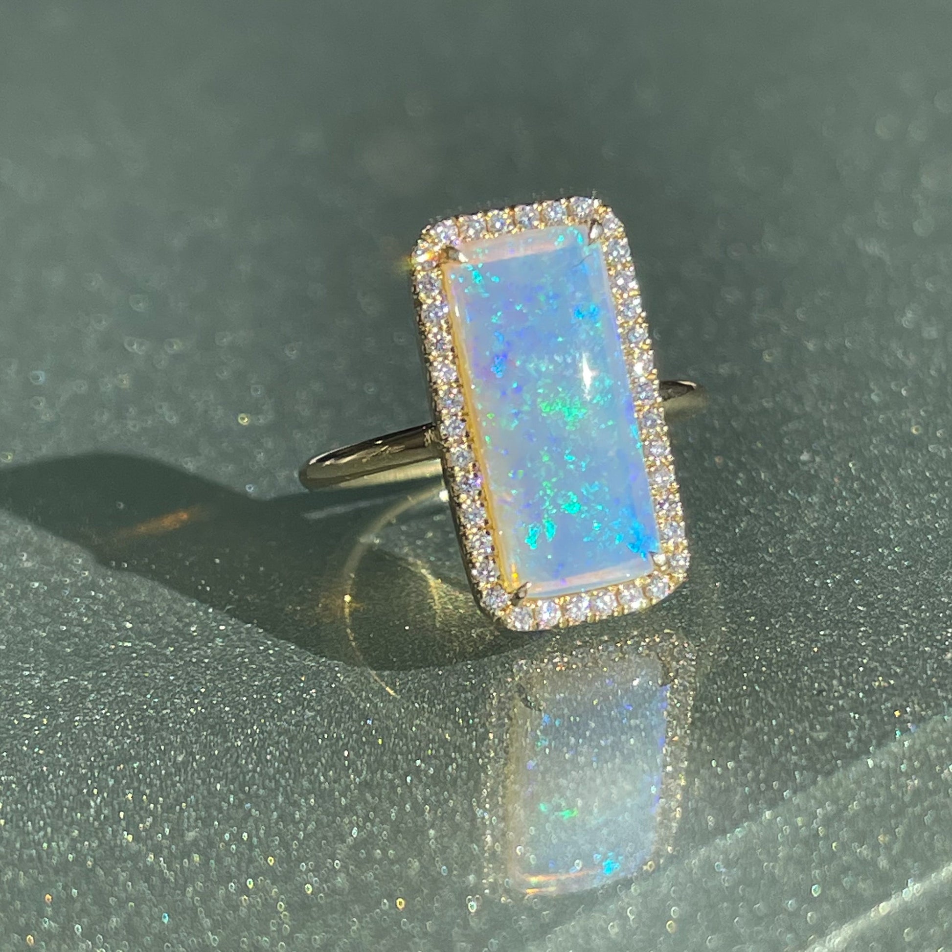 An Australian Opal Ring by NIXIN Jewelry resting on a tabletop. A blue green opal set in 14k yellow gold.