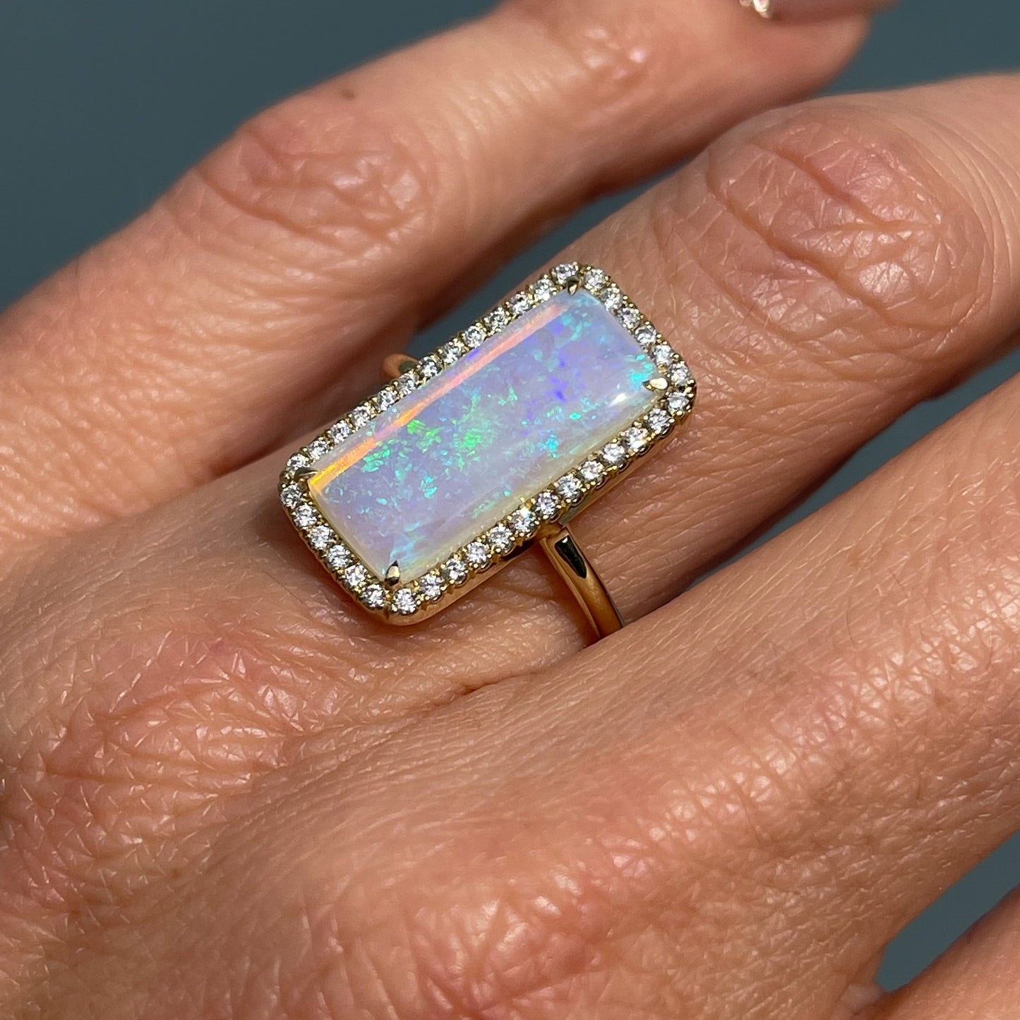 Close up shot of an Australian Opal Ring by NIXIN Jewelry modeled on the hand. Photo shows the lavender opal with green flash and surrounding diamond halo.