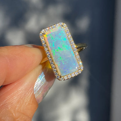 An Australian Opal Ring by NIXIN Jewelry with a diamond halo held in sunlight.
