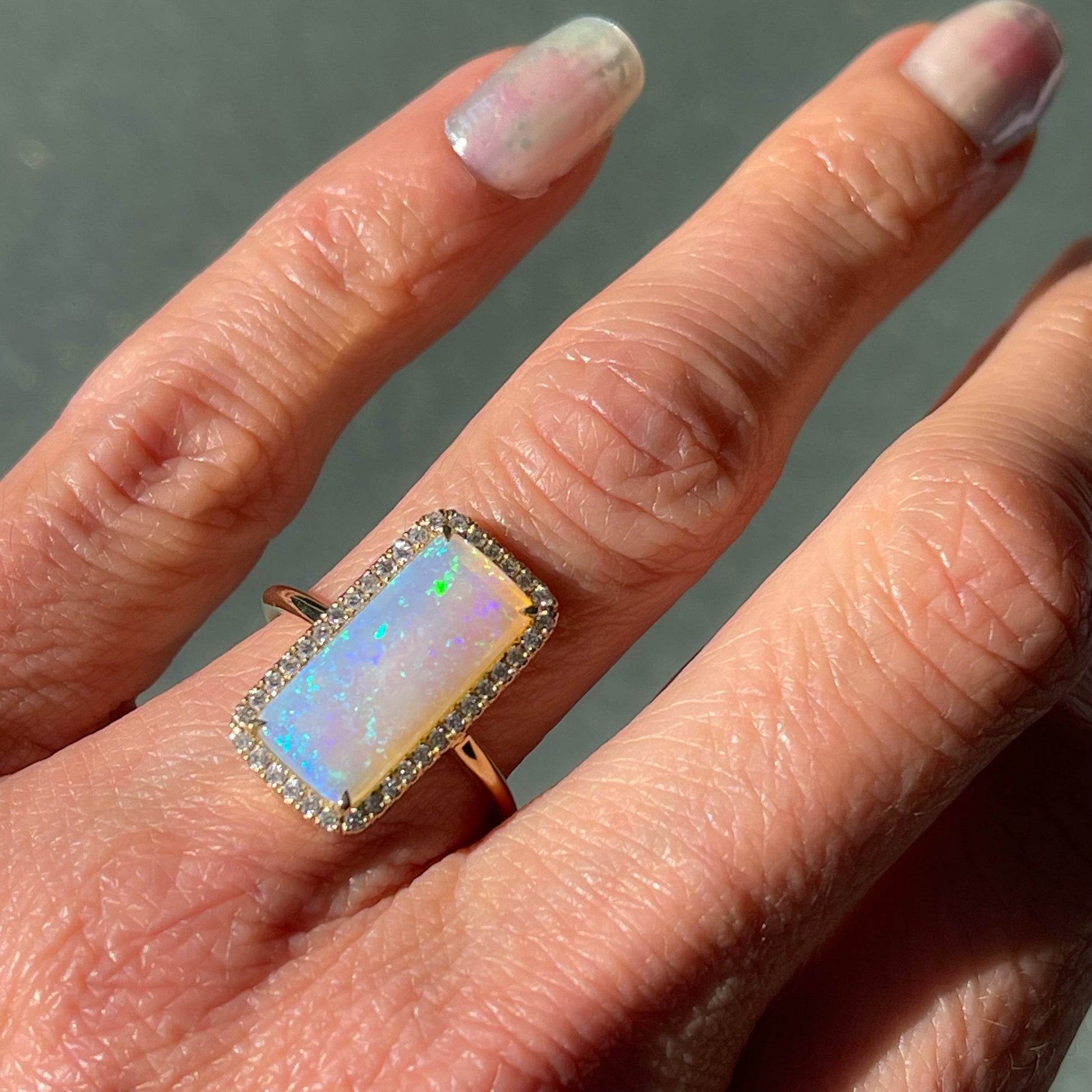 An Australian Opal Ring by NIXIN Jewelry modeled on the hand in fading light. An opal and diamond ring.