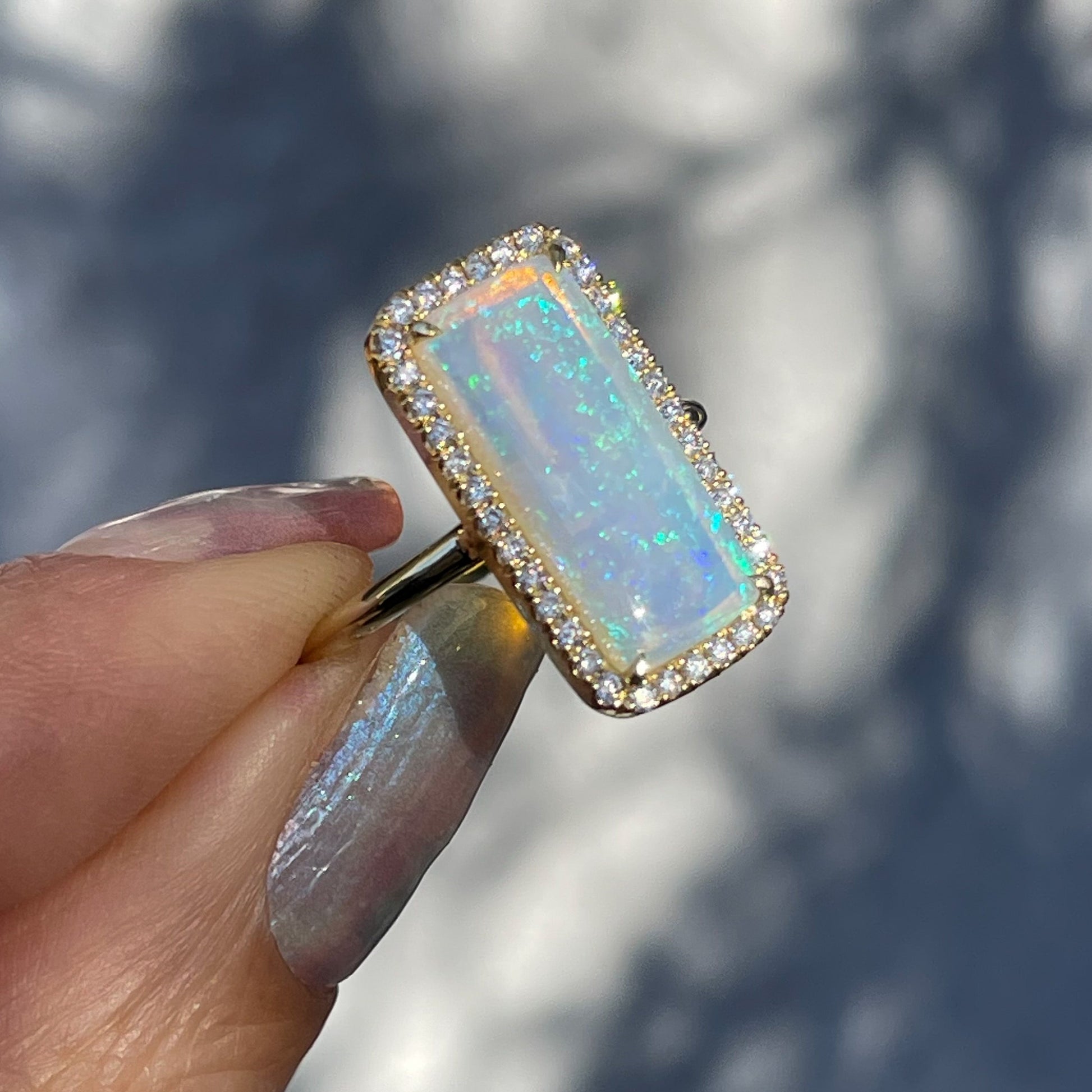 An Australian Opal Ring by NIXIN Jewelry shot at a side angle in front of a grey wall. An opal ring with diamonds.