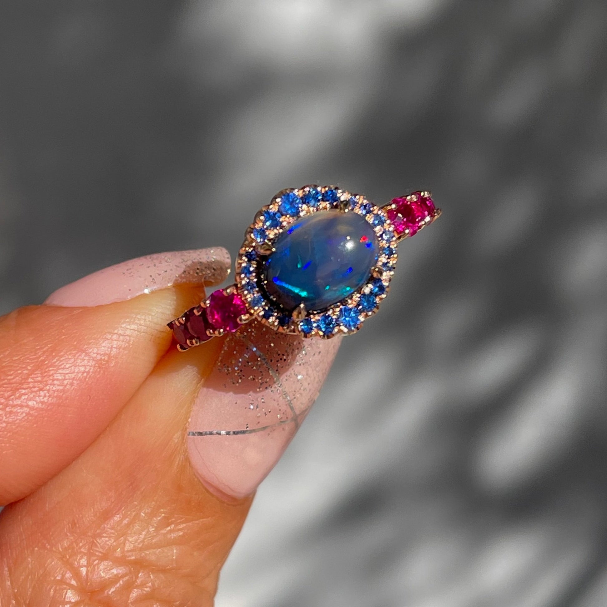 Sapphire and Opal Ring by NIXIN Jewelry held in sun. Australian black opal ring in rose gold.