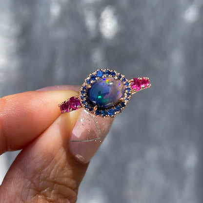 Sapphire and Opal Ring by NIXIN Jewelry held in front of grey wall. Opal and pink sapphire ring.