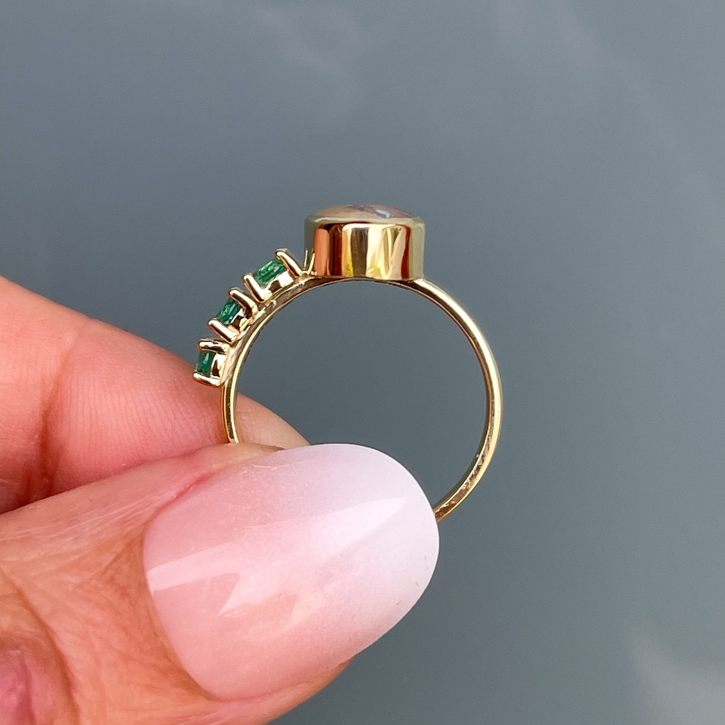Gold opal and emerald ring by NIXIN Jewelry held to show side